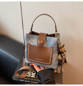 Detail of grey denim bucket bag with brown leather trim and retro woven shoulder strap