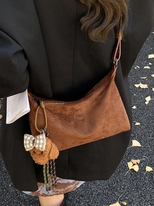 Brown suede crossbody bag with plush charm shown being worn outdoors in autumn style