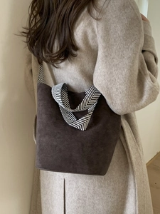 Brown suede bucket bag with herringbone strap worn by a model in an elegant wool coat
