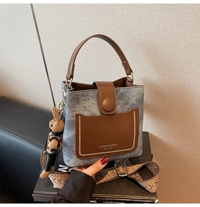 Detail of blue denim and brown leather bucket bag with a tribal weave strap and rabbit charm