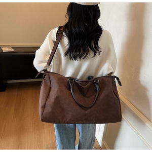 Détail d'un grand sac de voyage en daim marron foncé porté par un mannequin de dos