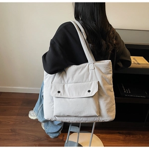 Detail of grey canvas tote bag featuring a large front flap pocket with black buttons