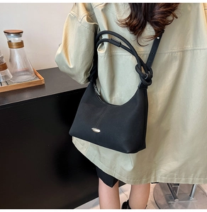 Detail of a black crescent shoulder bag with a unique knot strap and silver logo accent