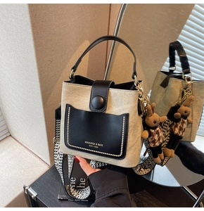 Detail of beige bucket bag featuring black pocket, gold studs and plush rabbit charm