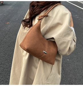 Detail of caramel brown half-moon underarm bag with knot strap and silver metal piece