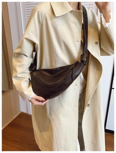 Detail of a dark brown crescent bag with a unique knot shoulder strap on a trench coat