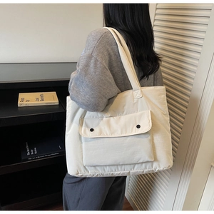 Detail of a large off-white canvas tote bag with front pocket and dual black snap buttons