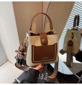 Detail of canvas bucket bag with brown leather trim, retro strap and plush bunny charm