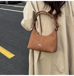 Detail of caramel suede crescent shoulder bag with knotted strap shown on a beige coat