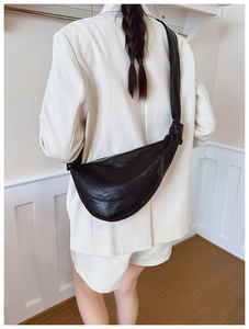 Rear view of a model wearing a black glossy leather crescent crossbody bag with white blazer