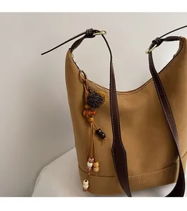 Détail d'un sac cabas en daim marron avec bandoulière en cuir et breloque à pompon ethnique