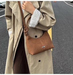 Brown suede hobo bag with silver oval buckle styled on a trench coat shoulder