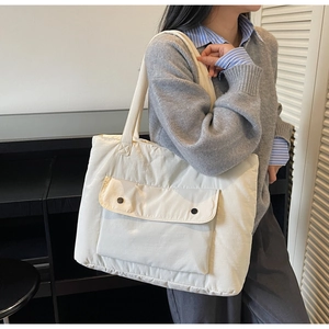 Close-up of a white quilted tote bag featuring a front pocket with black snap buttons