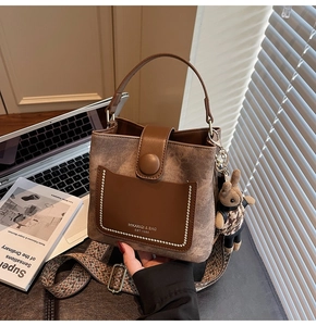 Close-up of brown suede bucket bag with pearl trim, wide ethnic strap and rabbit charm
