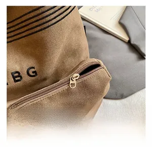 Close-up of brown canvas shoulder bag showing zipper detail and black embroidered lettering