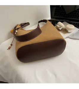 Détail du sac seau en daim avec surpiqûres contrastées et breloque à pampille en bois