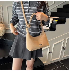 Chic beige suede crossbody bag with elegant knot strap and metal detail worn on stairs