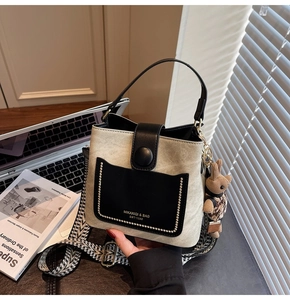 Detail of beige bucket bag with black flap, wide patterned strap and plush bear charm