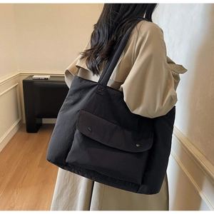 Detail of black large capacity tote bag featuring two front magnetic snap buttons and pockets