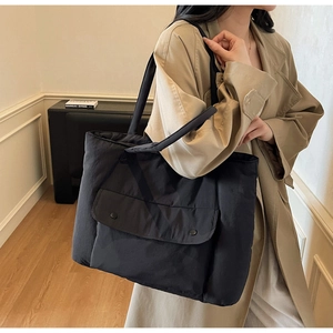 Detail of black canvas tote bag showing large front pocket with two round buttons