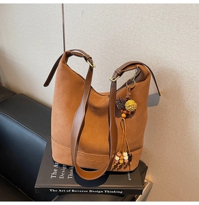 Sac seau en daim caramel avec pompon perlé et bandoulière en cuir sur des livres