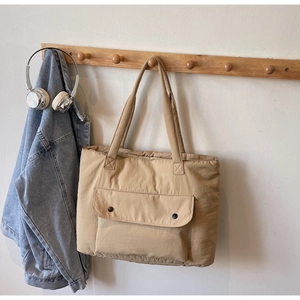 Close-up of khaki tote bag featuring large flap pocket and black dot fastener on wall hook