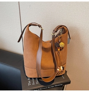 Détail d'un sac seau en daim marron avec bandoulière en cuir et pendentif à pompon
