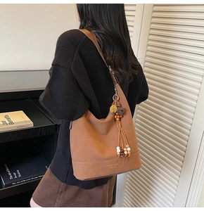 Détail du sac hobo en daim marron avec glands bohèmes, perles en bois et pompons