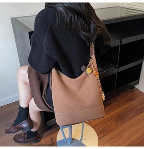 Détail d'un sac hobo en daim marron avec glands décoratifs et logo en feuille d'or