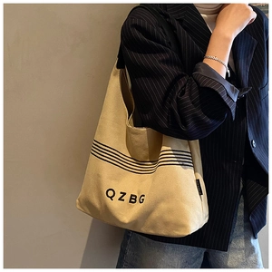 Detail of beige canvas tote with black stripes and QZBG lettering worn over the shoulder