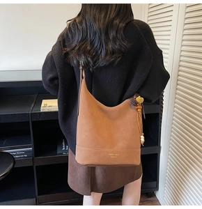 Détail d'un sac cabas en daim marron vintage avec un charme décoratif en peluche et perles