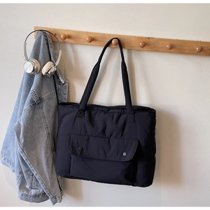 Detail of black nylon tote bag featuring a snap-button front pocket and long shoulder straps