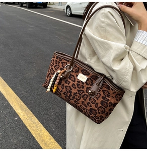 Detail of leopard print tote bag with wooden bead charm and metallic logo plate