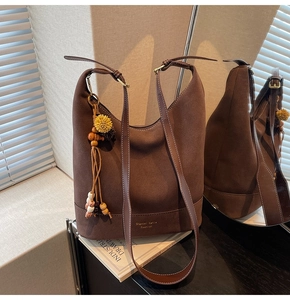 Détail macro du sac hobo en daim marron foncé avec pompon ethnique et détails dorés