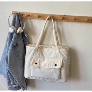 Detail of a large beige canvas tote bag with a front buttoned flap pocket on a wooden hook