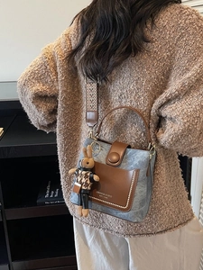 Blue denim bucket bag with brown leather details and a cute bunny charm on a model