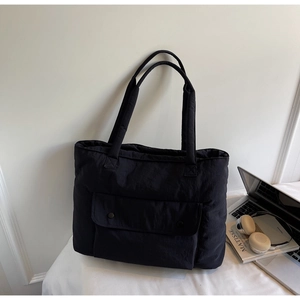 Detail view of a large black padded tote bag with multiple pockets on a stylish workspace