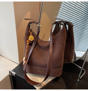 Détail du sac cabas en daim avec pendentif perlé et logo de marque sur bois