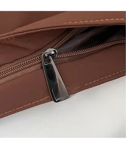 Detailed macro view of dark glossy metal zipper puller on brown embroidered canvas bag