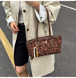 Detail of leopard print tote bag with metallic logo plate and colorful beaded tassel