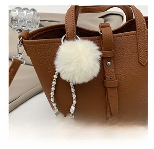 Dettaglio del ciondolo a pompon bianco con catena di perle su borsa a secchiello in pelle marrone