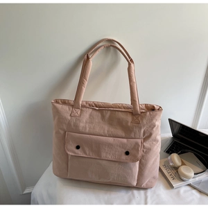 Close-up of pink nylon tote bag with front pocket and round buckle on a desk