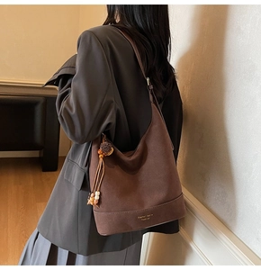 Détail du sac hobo en daim marron mat avec pompon et pendentif décoratif en bois