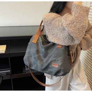 Close-up of a dark grey canvas tote bag featuring brown leather details and logo patch
