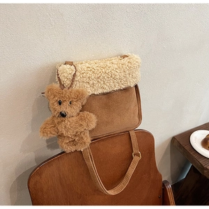 Dettaglio borsa a tracolla in pelle scamosciata marrone con patta in shearling e ciondolo orsetto