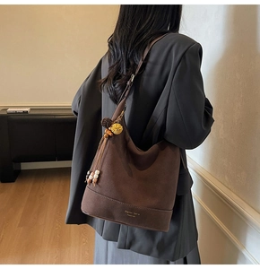 Détail du sac hobo en daim marron mat avec pompon décoratif et bandoulière réglable