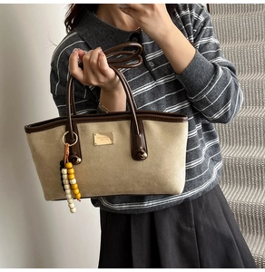 Detail of canvas tote bag with brown leather trim and colorful beaded charm accessory