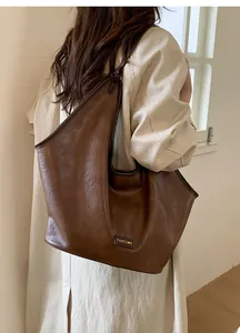 Brown vintage leather hobo bag with wide strap and metal logo worn by a model