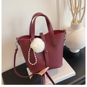 Dettaglio borsa a secchiello bordeaux in pelle granata con catena di perle e pompon