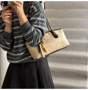 Detail of beige suede bag with brown leather trim and colorful wooden bead charm